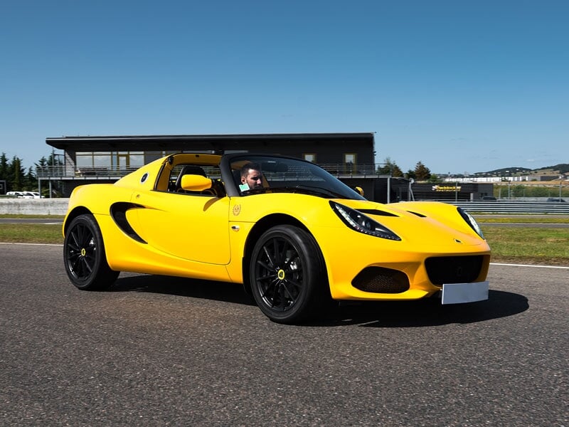Lotus Elise Sport jaune sur circuit asphalte à Andrézieux, avec un pilote concentré au volant sous un ciel bleu clair.