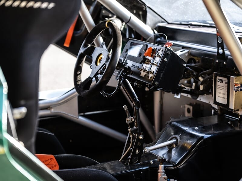 Intérieur d'une Mitjet 2L avec volant, siège baquet et tableau de bord technique détaillé.