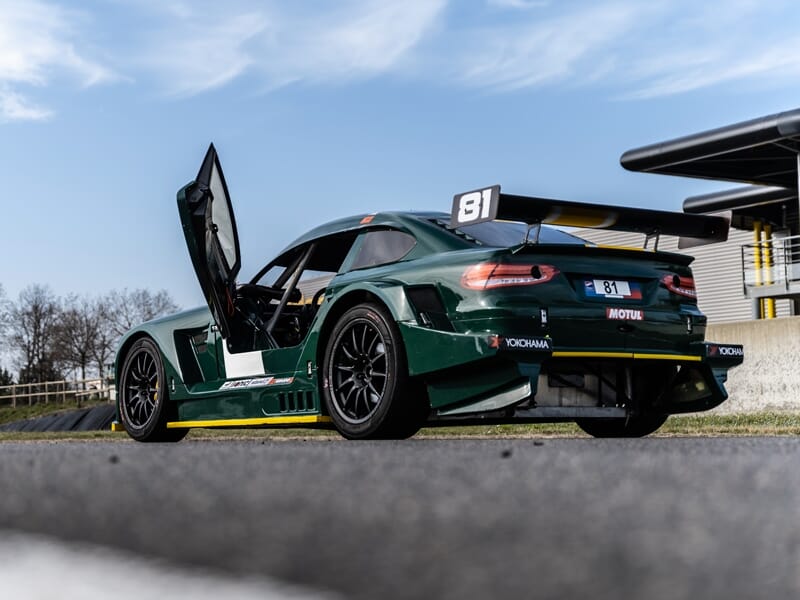 Mitjet 2L verte avec portes papillon ouvertes, stationnée sur une piste d'asphalte.