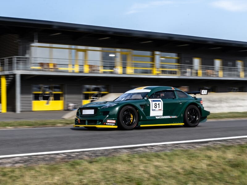Voiture de course verte Mitjet 2L en mouvement rapide sur circuit, avec numéro 81 visible sur la portière.
