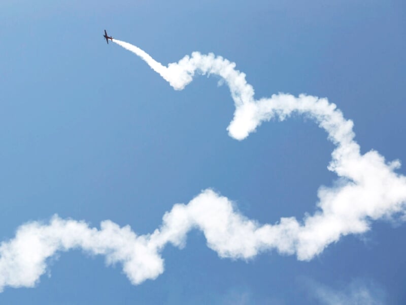 Avion de voltige effectuant une figure acrobatique dans le ciel, laissant une traînée de fumée blanche en spirale.