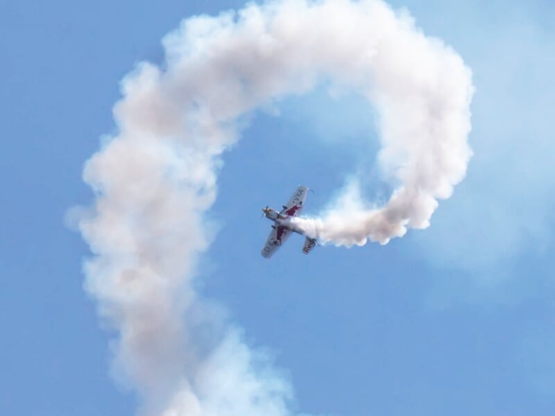 Avion de voltige réalisant une figure en boucle dans le ciel, laissant une traînée de fumée blanche.