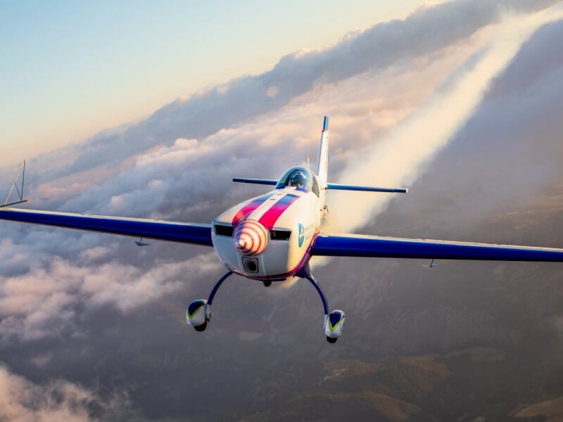 Avion de voltige en vol au-dessus des nuages, avec un ciel aux couleurs chaudes du coucher de soleil.
