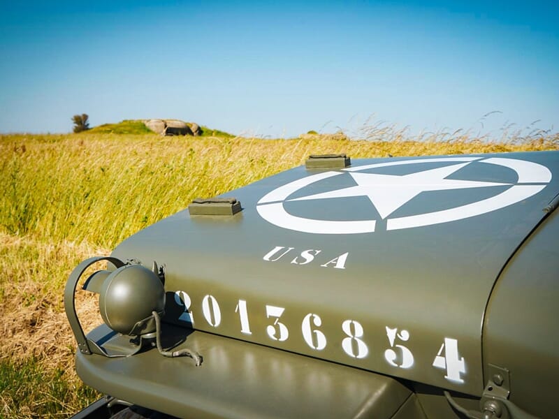 Gros plan sur le capot d'une jeep militaire vintage avec une étoile blanche et l'inscription USA dans un champ.