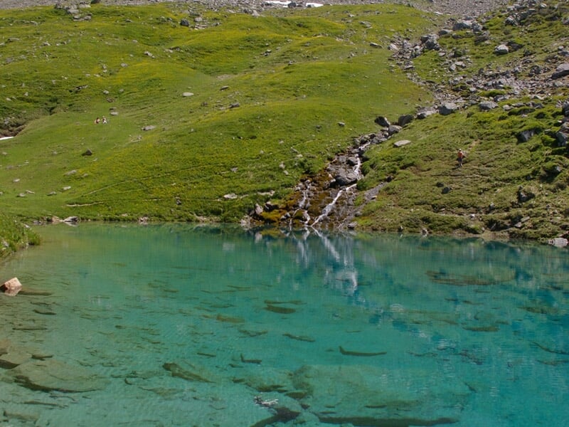 Lac de montagne aux eaux turquoise entouré de prairies vertes et de rochers.