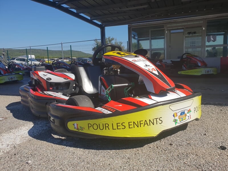 Un kart rouge et blanc avec l'inscription pour les enfants est garé sur un sol en gravier sous un abri.