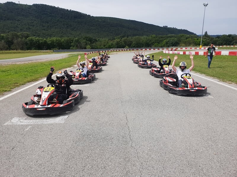 Un groupe de pilotes en karts alignés sur une piste de karting, certains avec les bras levés en signe de victoire.