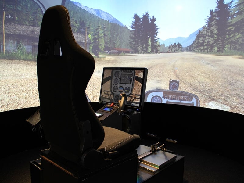 Siège de pilote dans un simulateur d'avion avec écran large affichant un paysage montagneux et une route.