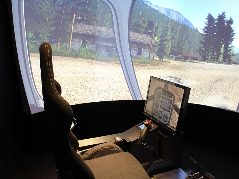 Siège de simulateur d'avion face à un écran incurvé affichant une route en forêt avec montagnes en arrière-plan.