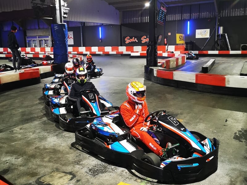 Quatre pilotes en karting alignés sur la piste intérieure, portant des casques et des combinaisons de course.
