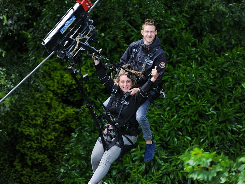 Un homme et une femme faisant un saut à l'élastique, avec un sourire joyeux, devant un fond de feuillage dense et vert