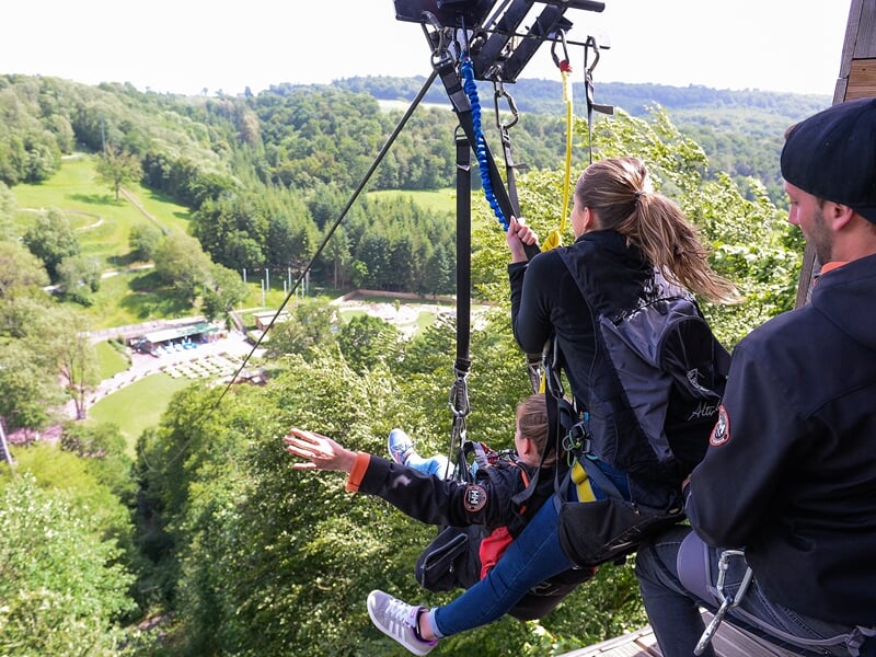 Deux personnes sur une plateforme de saut à l'élastique, dont une étendant ses bras comme pour voler au-dessus d'un paysage verdoyant
