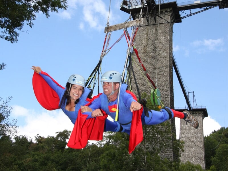 Deux personnes déguisées en super-héros, souriantes et étendues bras ouverts lors d'un saut à l'élastique