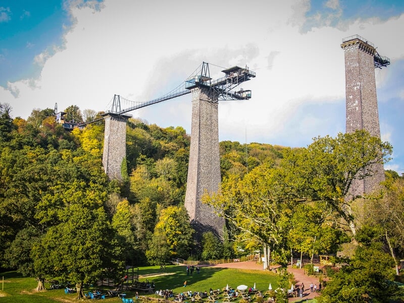 Vue panoramique d'un grand viaduc avec deux tours de pierre, entouré de forêts verdoyantes et d'un parc avec des gens