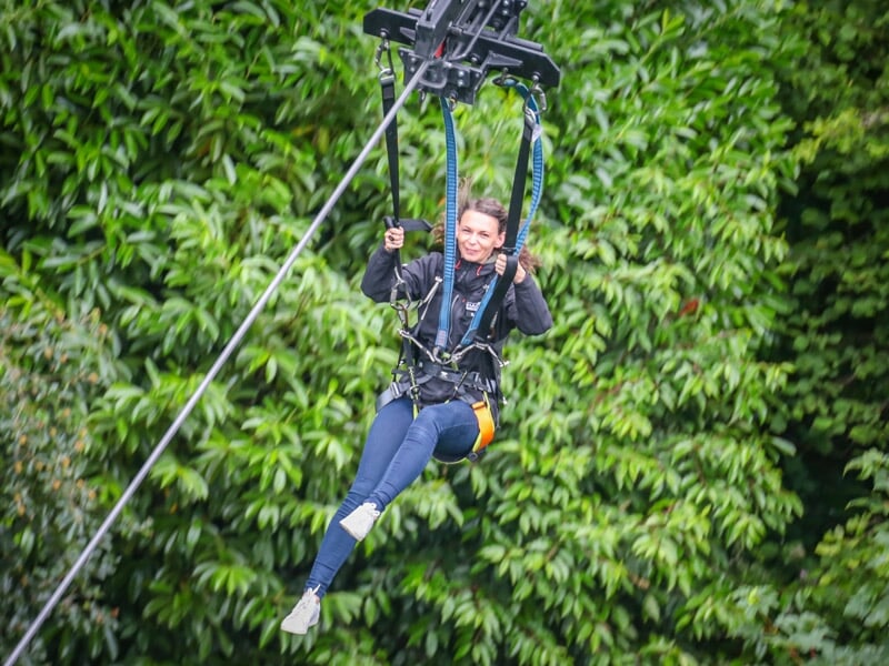 Une femme souriante effectuant un saut à l'élastique, suspendue à un harnais contre un fond de feuillage vert dense