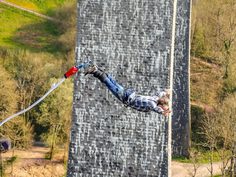 Une personne en saut à l'élastique, étendue horizontalement avec un mur en pierre texturé en arrière-plan
