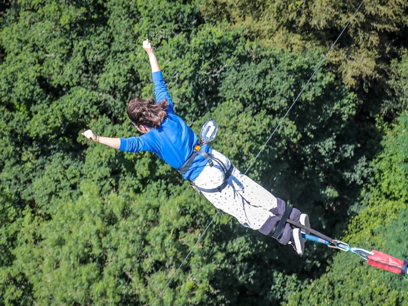 Une personne en mouvement lors d'un saut à l'élastique, avec une vue sur la forêt en arrière-plan
