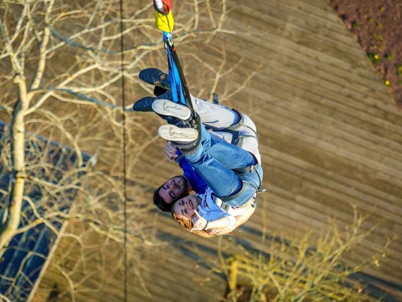 Un couple accroché à un saut à l'élastique en tandem, en chute libre au-dessus d'un sol en bois