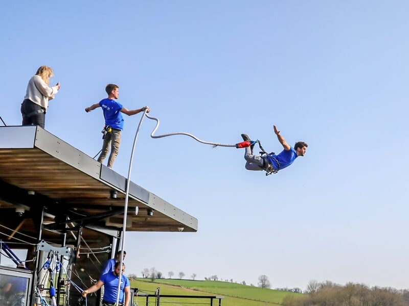 Un homme en train de sauter d'une plateforme élevée lors d'un saut à l'élastique, avec des spectateurs derrière lui