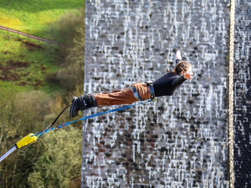 Une personne en saut à l'élastique, plongée vers le sol avec un grand mur en briques en arrière-plan