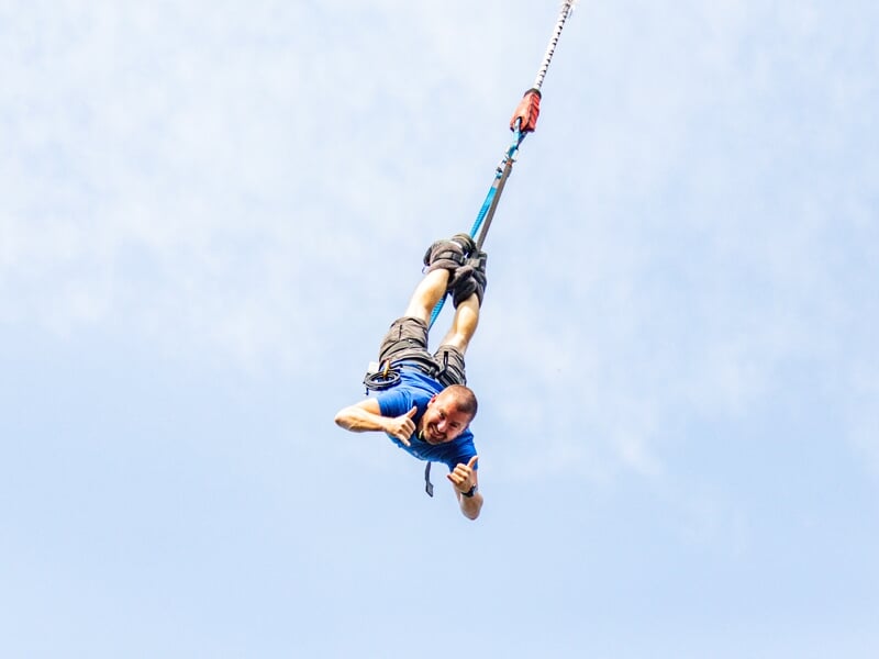 Une personne en plein saut à l'élastique, vue du dessous, avec le ciel bleu clair en arrière-plan