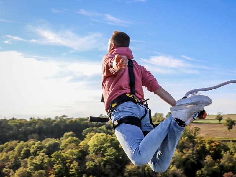 Un homme en pull rose faisant un saut à l'élastique et tendant la main vers l'appareil photo