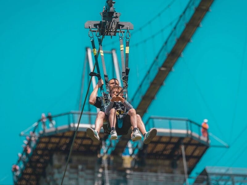 Personne en train de faire un saut élastique à La Ferrière Harang, suspendue par un harnais avec ciel bleu en arrière-plan.