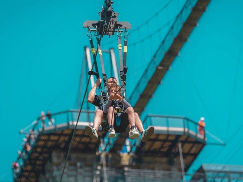 Personne en train de faire un saut élastique à La Ferrière Harang, suspendue par un harnais avec ciel bleu en arrière-plan.