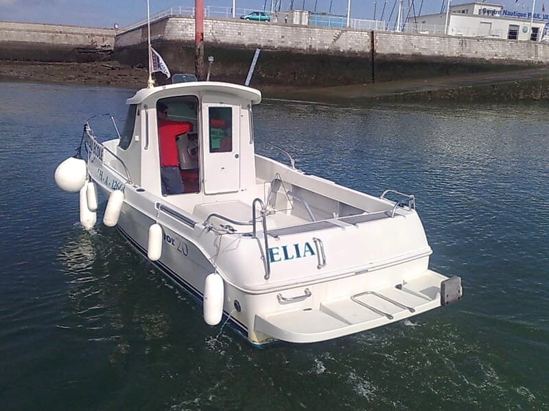 Petit bateau blanc amarré près d'un quai avec des bouées blanches et un mur en arrière-plan.