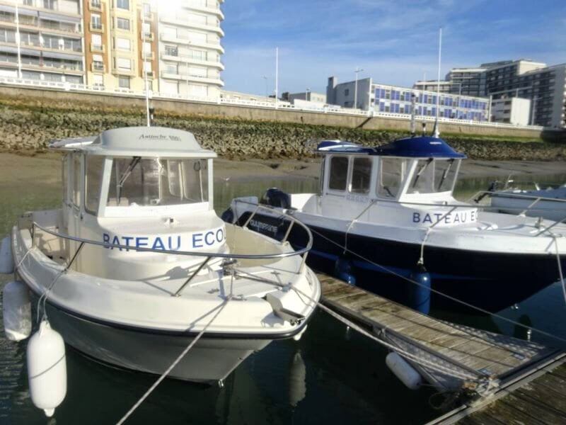 Deux bateaux blancs amarrés côte à côte dans un port avec des bâtiments en arrière-plan.