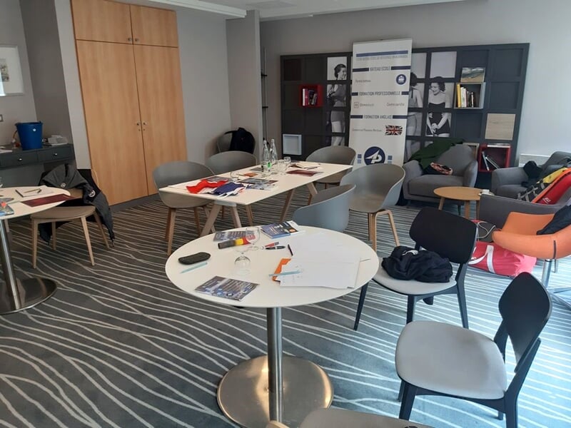 Salle de réunion avec plusieurs personnes assises autour de tables, regardant un écran de projection.