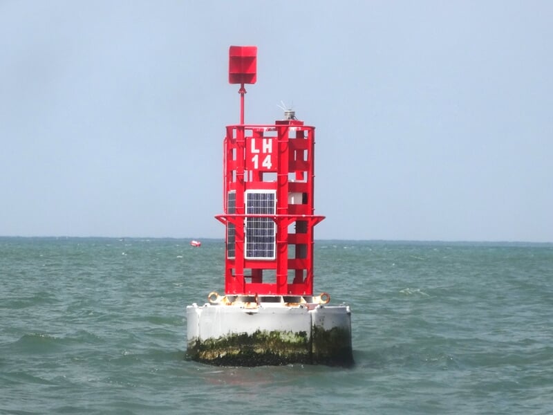 Bouée rouge flottant sur une mer calme sous un ciel clair, avec horizon visible au loin.