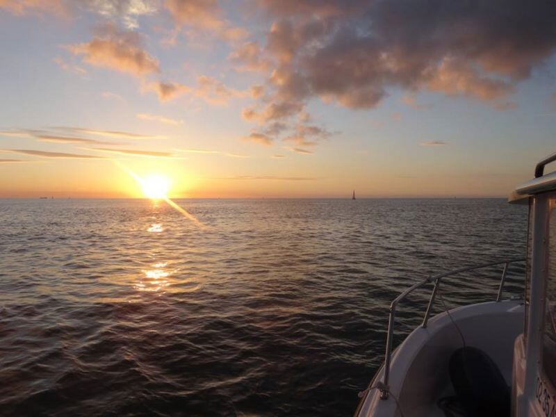 Soleil couchant sur la mer avec un bateau visible à droite et un ciel partiellement nuageux.