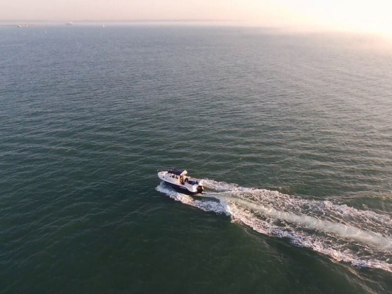 Bateau rapide sur une mer calme, vu de haut, laissant une traînée blanche derrière lui.