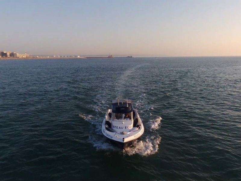 Bateau blanc vu de l'arrière naviguant sur une mer calme avec un ciel clair au coucher du soleil.