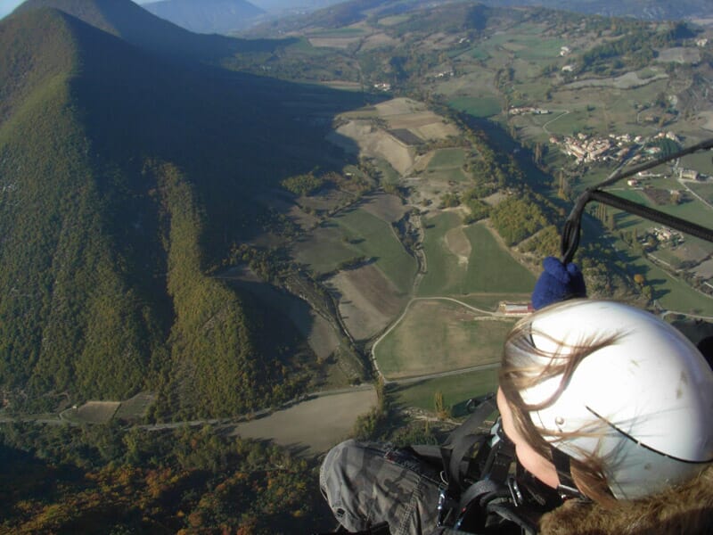 Paysage vallonné avec des champs et des collines, vu depuis un parapente, casque blanc de l'utilisateur visible.