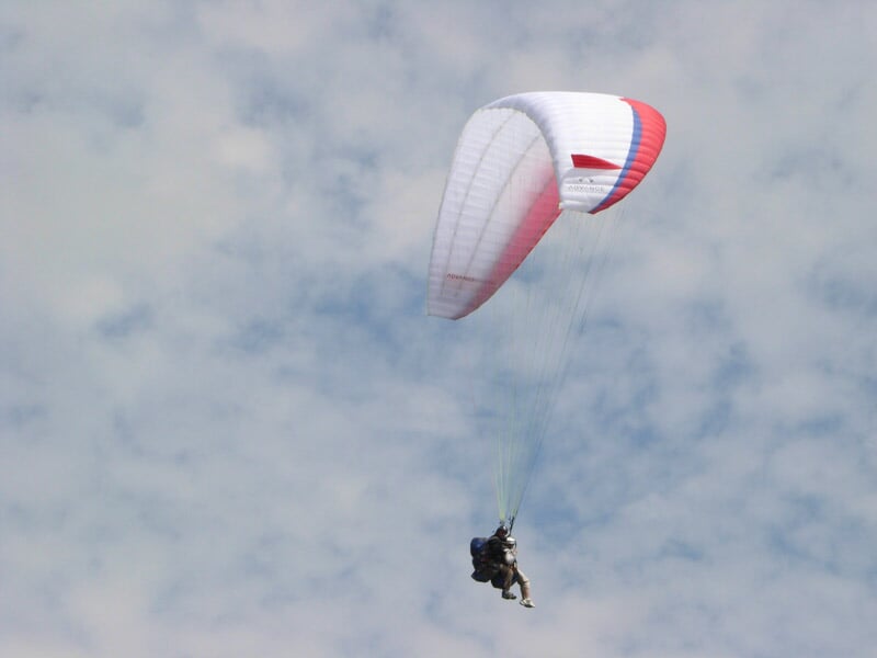 Parapente blanc et rouge flottant sous un ciel nuageux, avec un pilote en tandem.