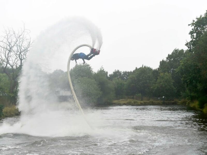 Un homme en flyboard réalise une figure acrobatique avec un jet d'eau puissant sur un lac.