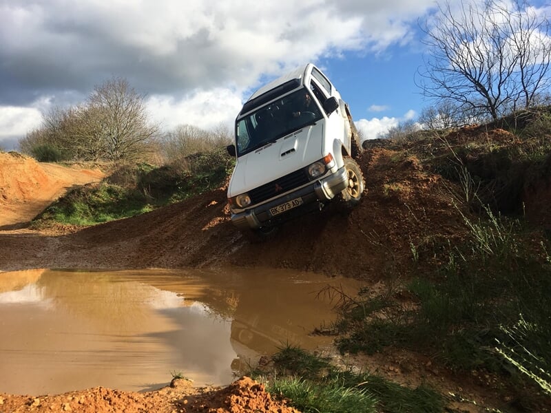 Un 4x4 blanc descend une pente boueuse dans un terrain tout-terrain avec des flaques d'eau.