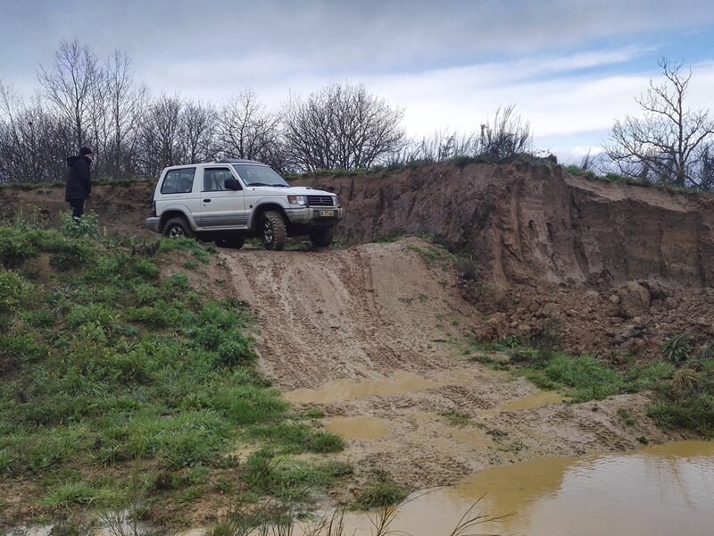 Un 4x4 blanc descend une pente raide dans un terrain accidenté avec de la boue et des flaques d'eau.