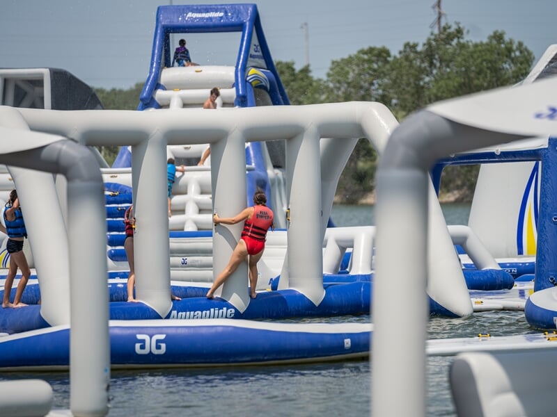 Jeunes filles s'amusent sur un parcours gonflable aquatique bleu et blanc avec des obstacles sur un lac.