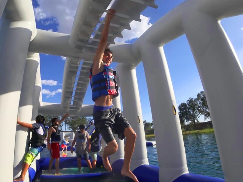 Jeunes filles grimpent et jouent sur un parcours gonflable aquatique bleu et blanc sur un lac.