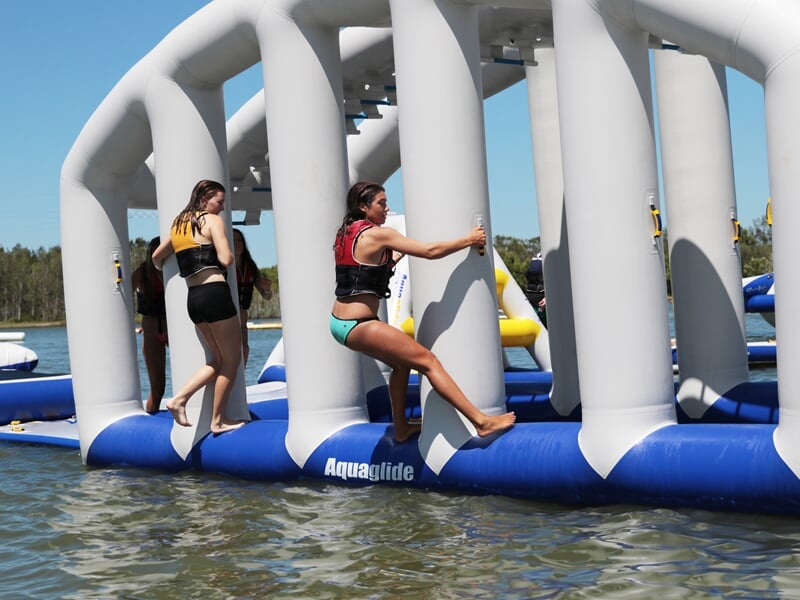 Jeunes filles s'amusent sur un parcours gonflable aquatique bleu et blanc avec des colonnes et des barres.
