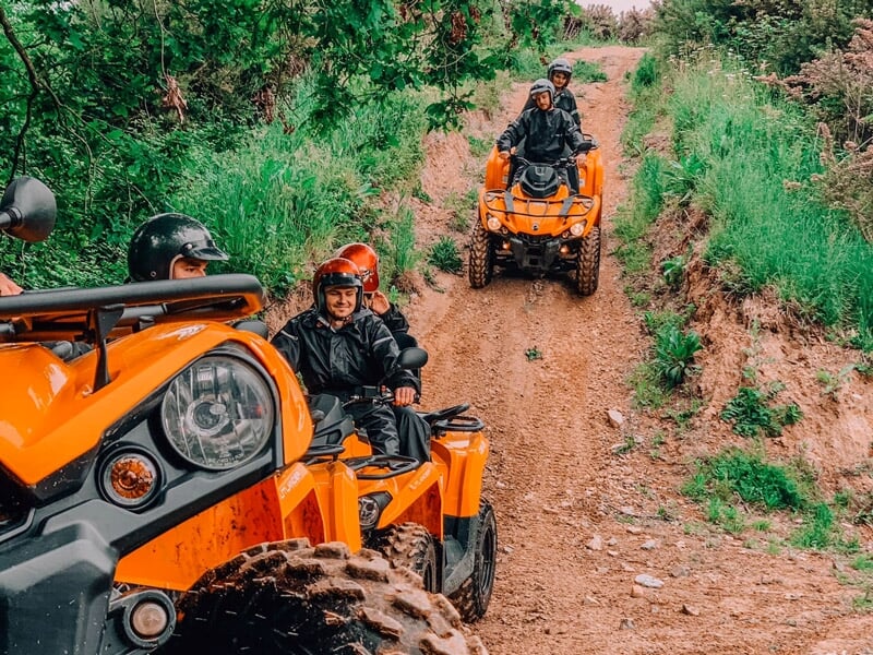 Groupe de personnes en quads oranges roulent sur un chemin de terre entouré d'arbres verts.