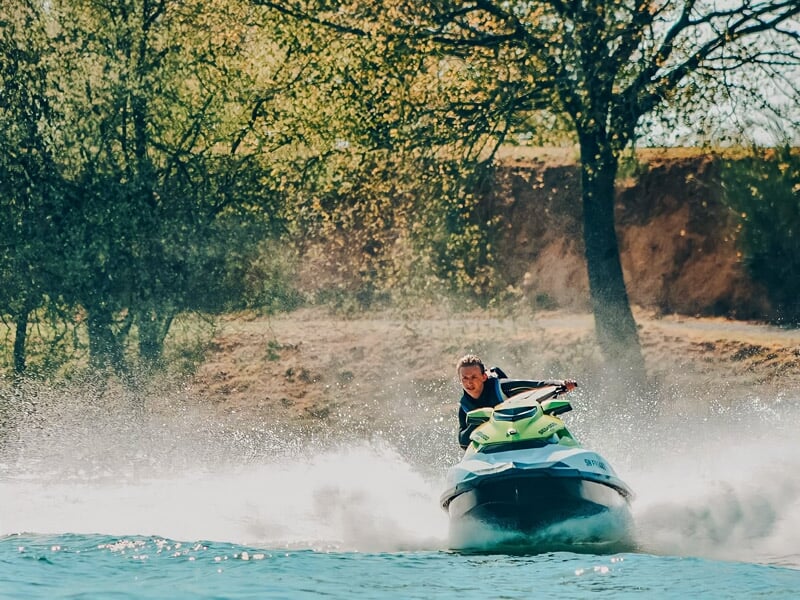 Personne en gilet de sauvetage conduit un jetski vert vif sur un lac, créant un grand sillage d'eau.