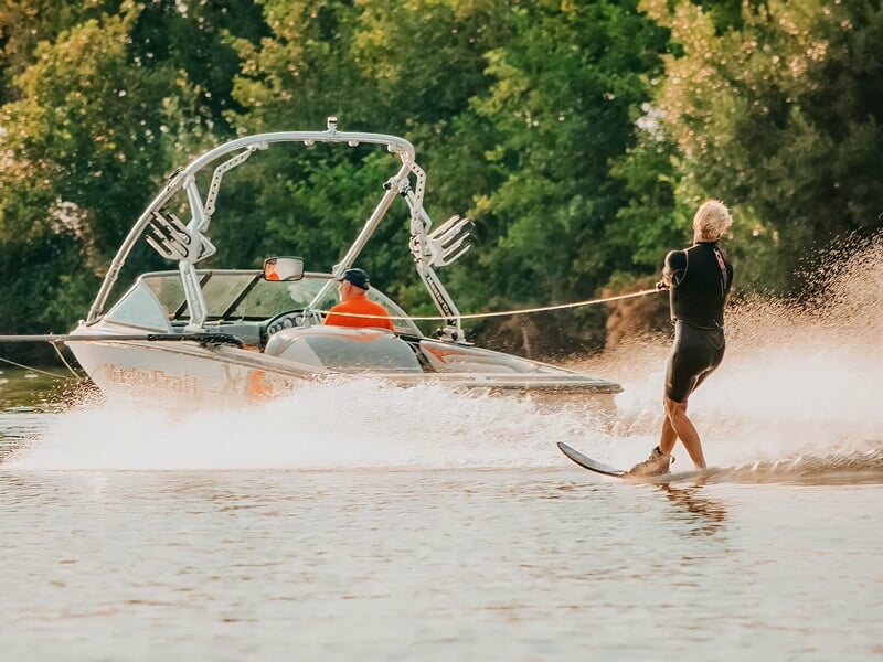 Un skieur nautique en gilet de sauvetage est tracté par un bateau sur un lac calme.