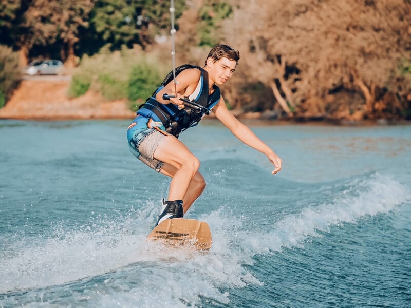 Un jeune homme pratique le wakeboard sur un lac, tiré par un bateau sous un ciel clair.