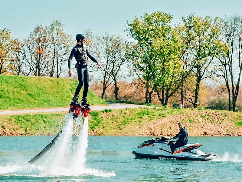 Un homme en flyboard s'élève au-dessus d'un lac, propulsé par de puissants jets d'eau.