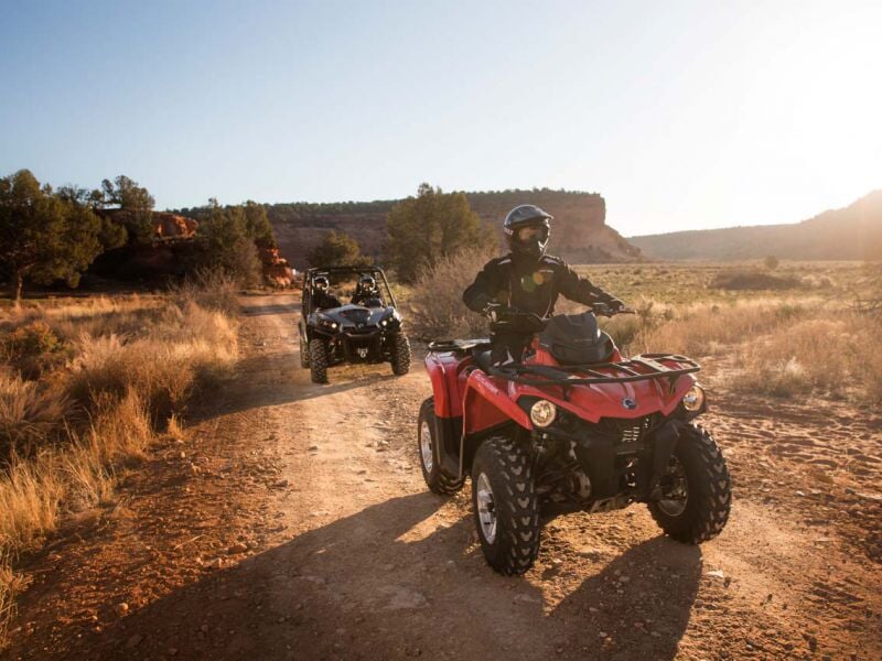 Un groupe de personnes en casques conduisent des quads rouges sur un chemin de terre en pleine nature.