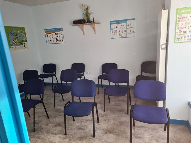 Salle de formation maritime avec chaises alignées, murs décorés de posters pédagogiques sur la signalisation nautique, ambiance simple et fonctionnelle.